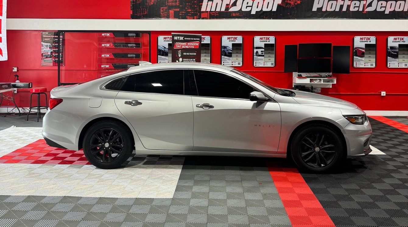 A silver car is parked in a garage with a checkered floor.