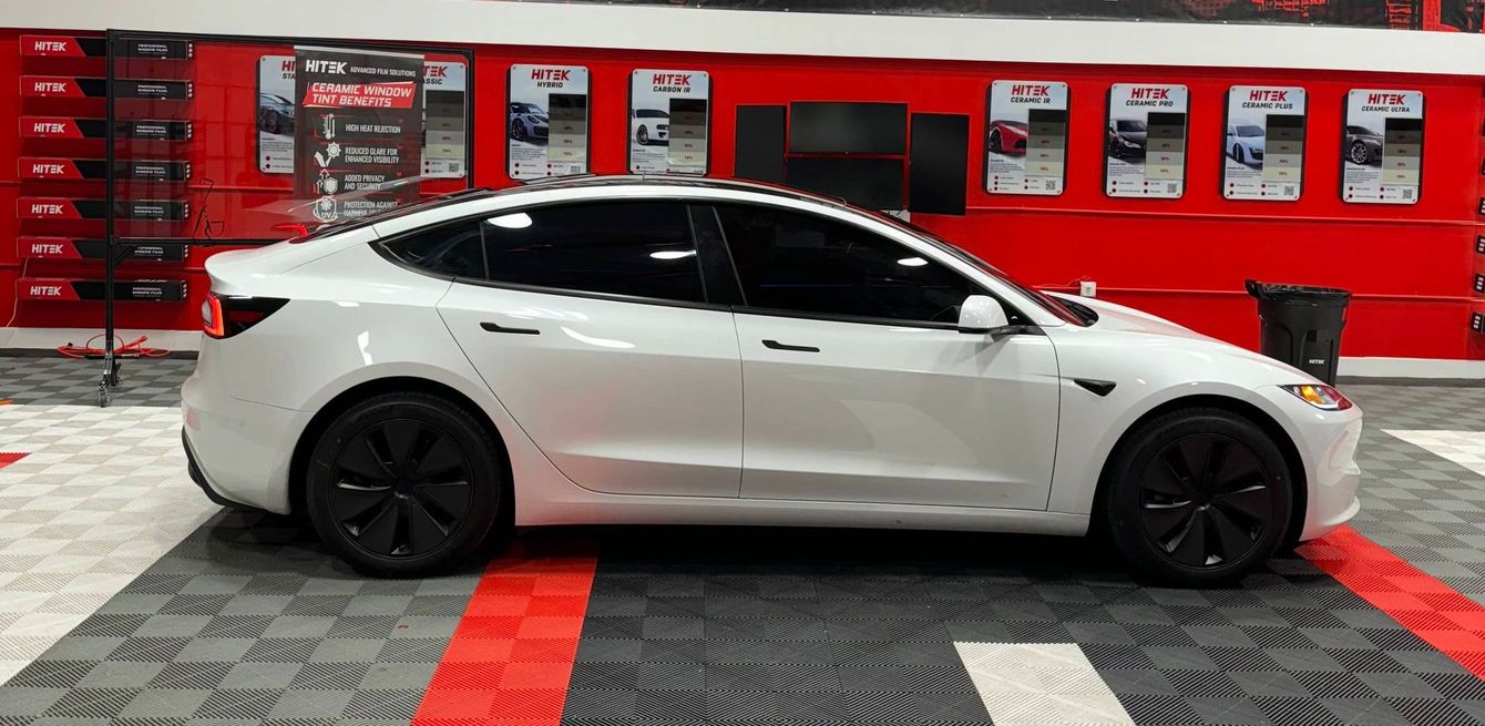 A white tesla model 3 is parked in a garage.