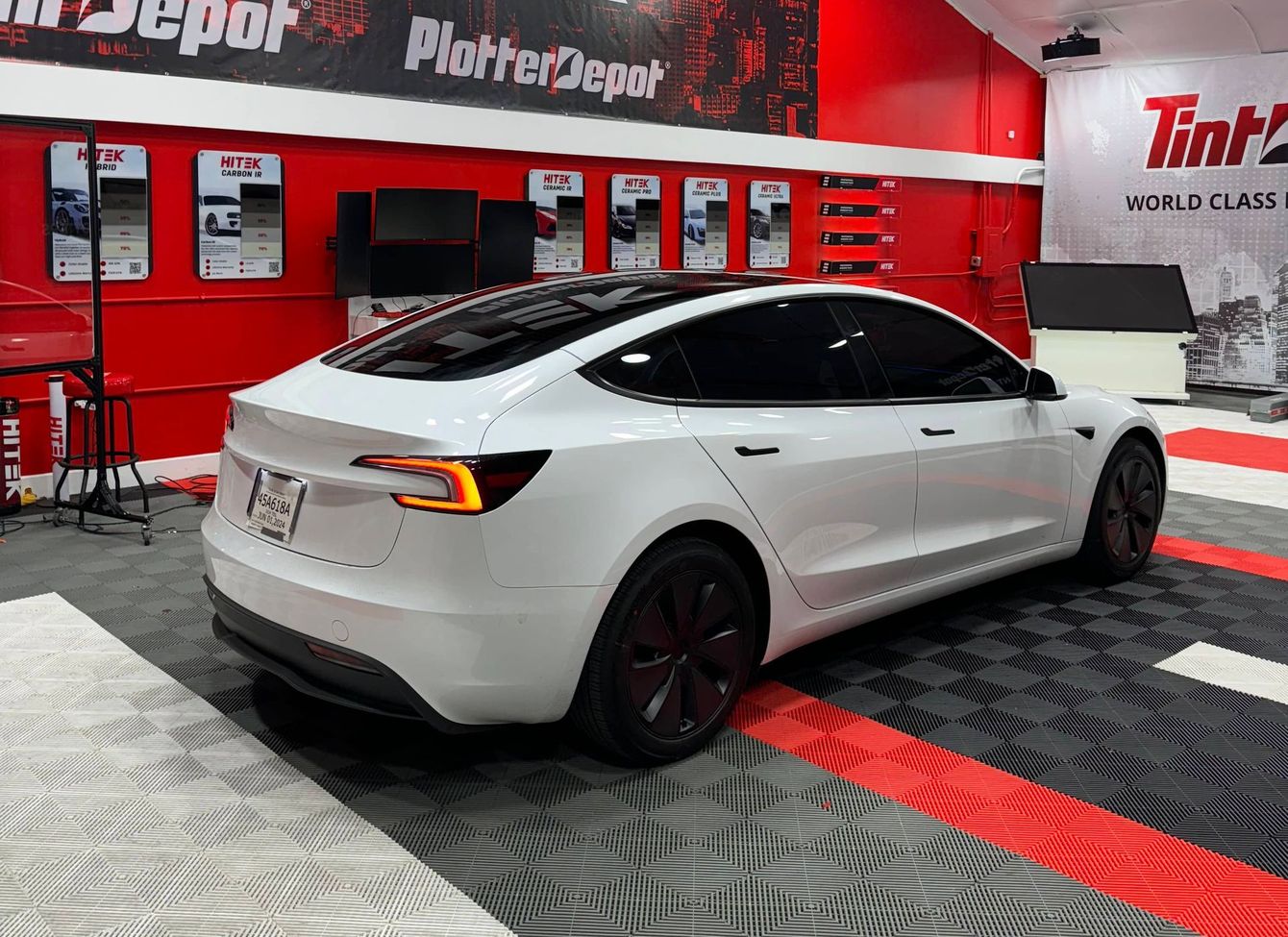 A white tesla model 3 is parked in a garage.