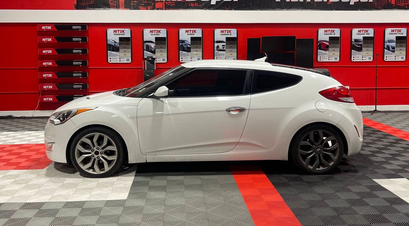 A white hyundai veloster is parked in a car showroom.