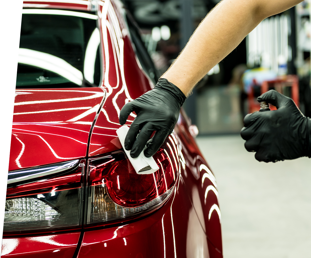 A man wearing gloves is working on a red car. A man wearing gloves is working on a red car.