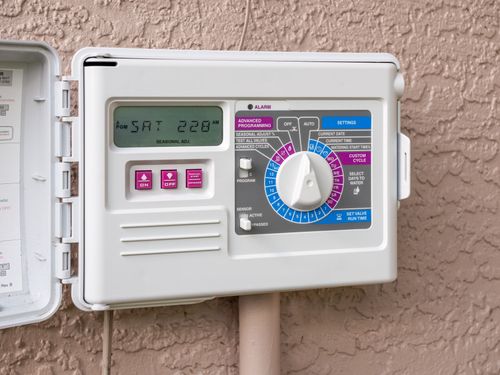 Outdoor sprinkler timer control panel with digital display and rotary dial mounted on a wall