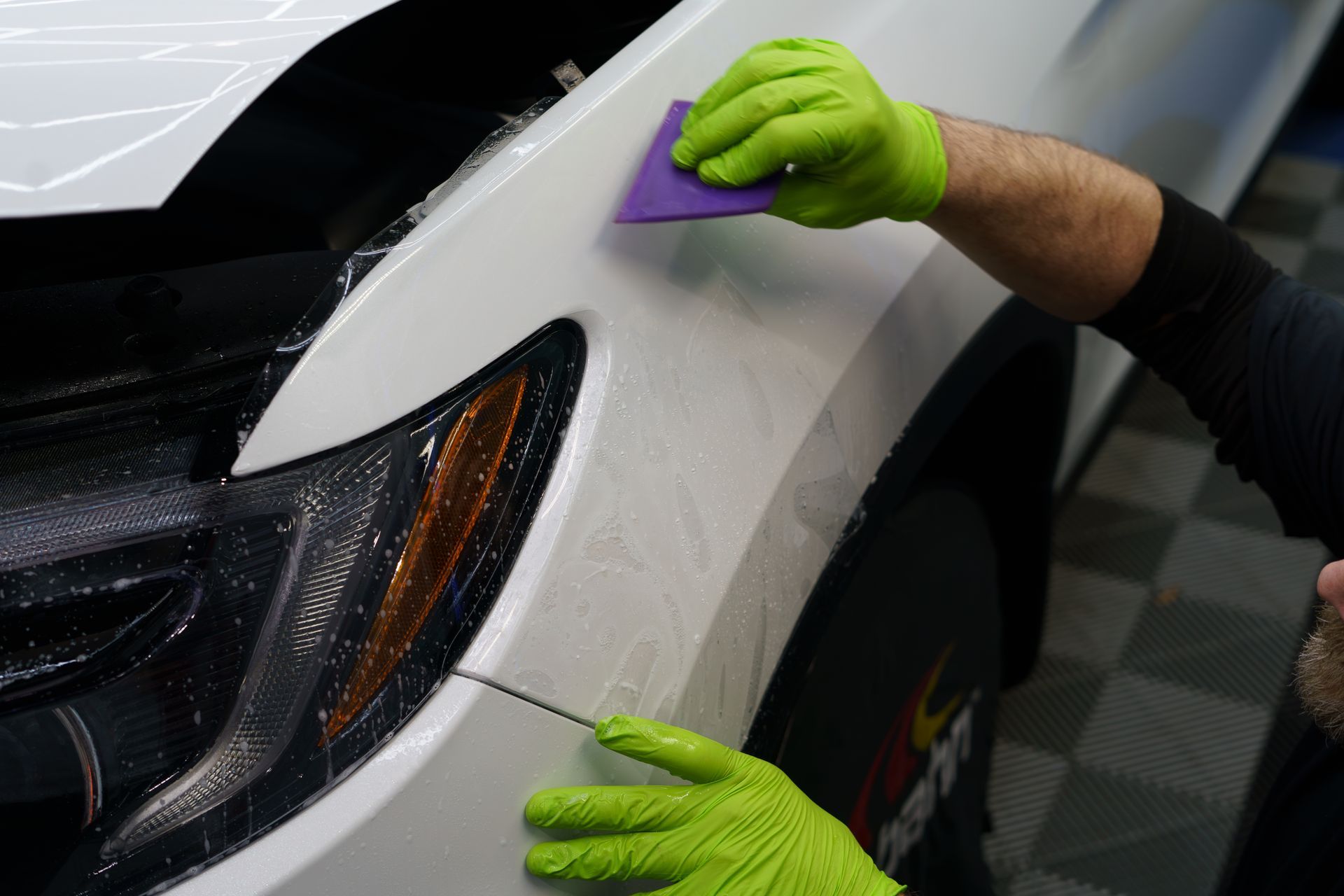 A person wearing green gloves is cleaning the front of a white car.