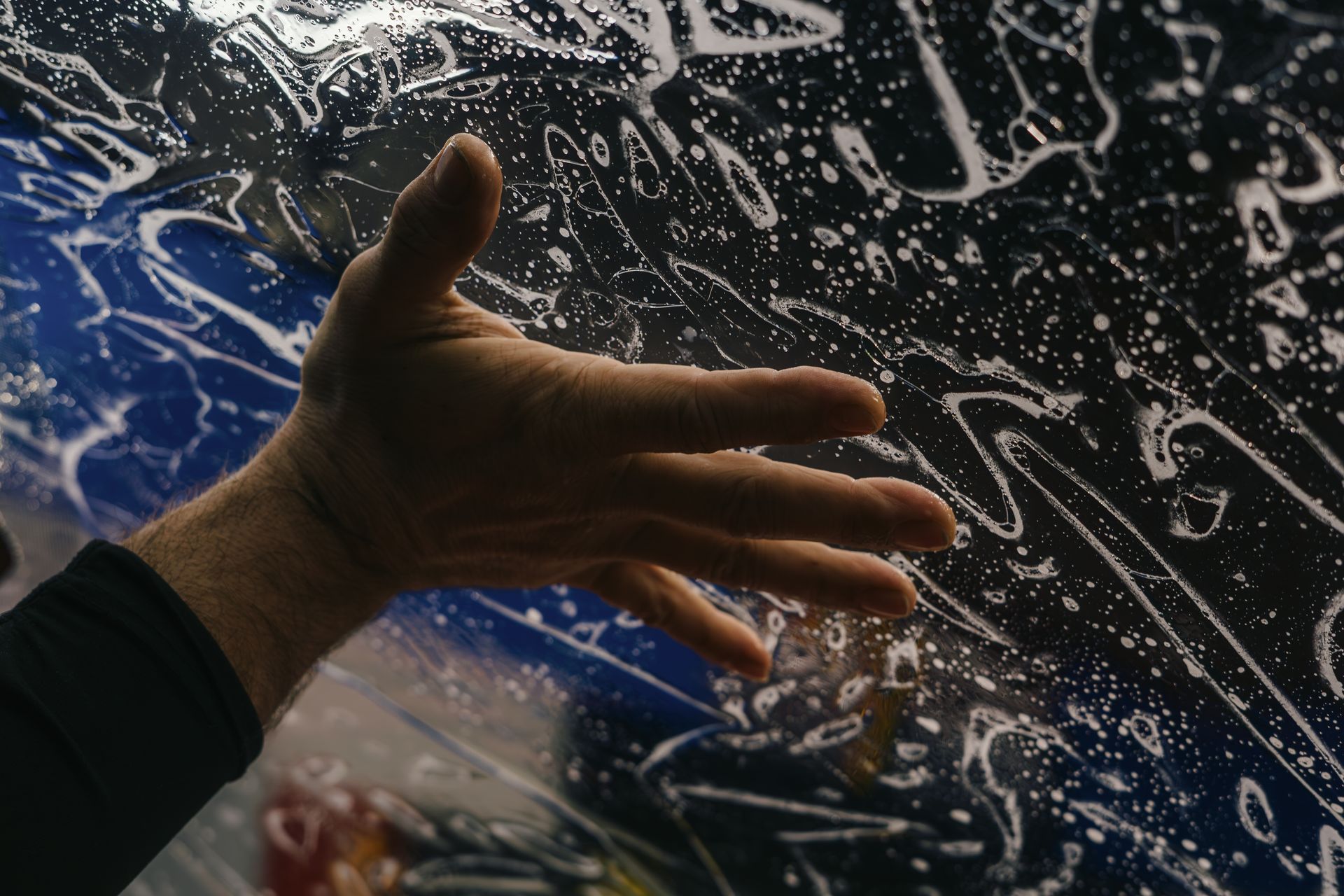 Hand smoothing soapy film on a blue surface; preparing for application.