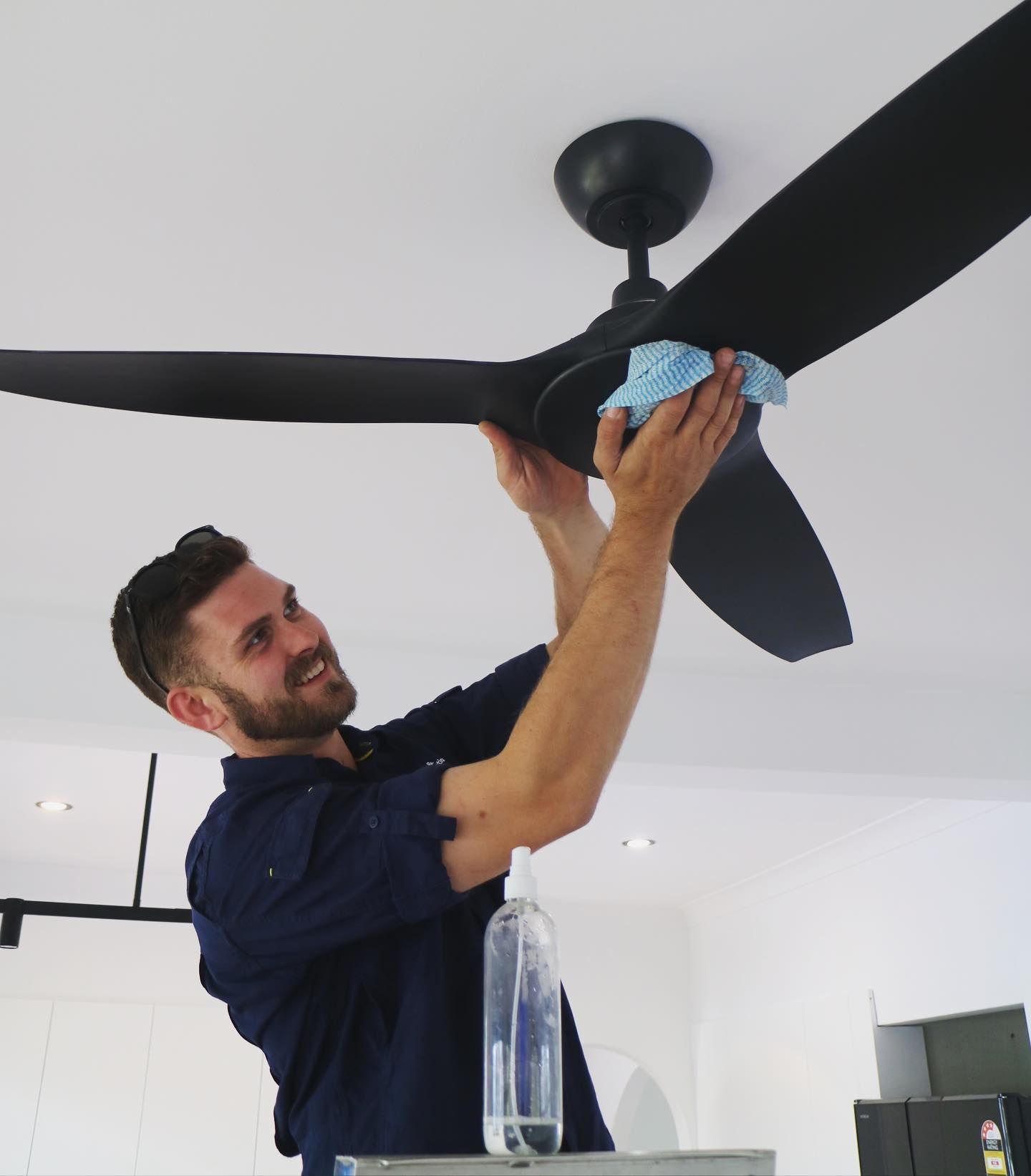 Electrician finalising ceiling fan installation — TB Electrical & Communications in Erina, NSW