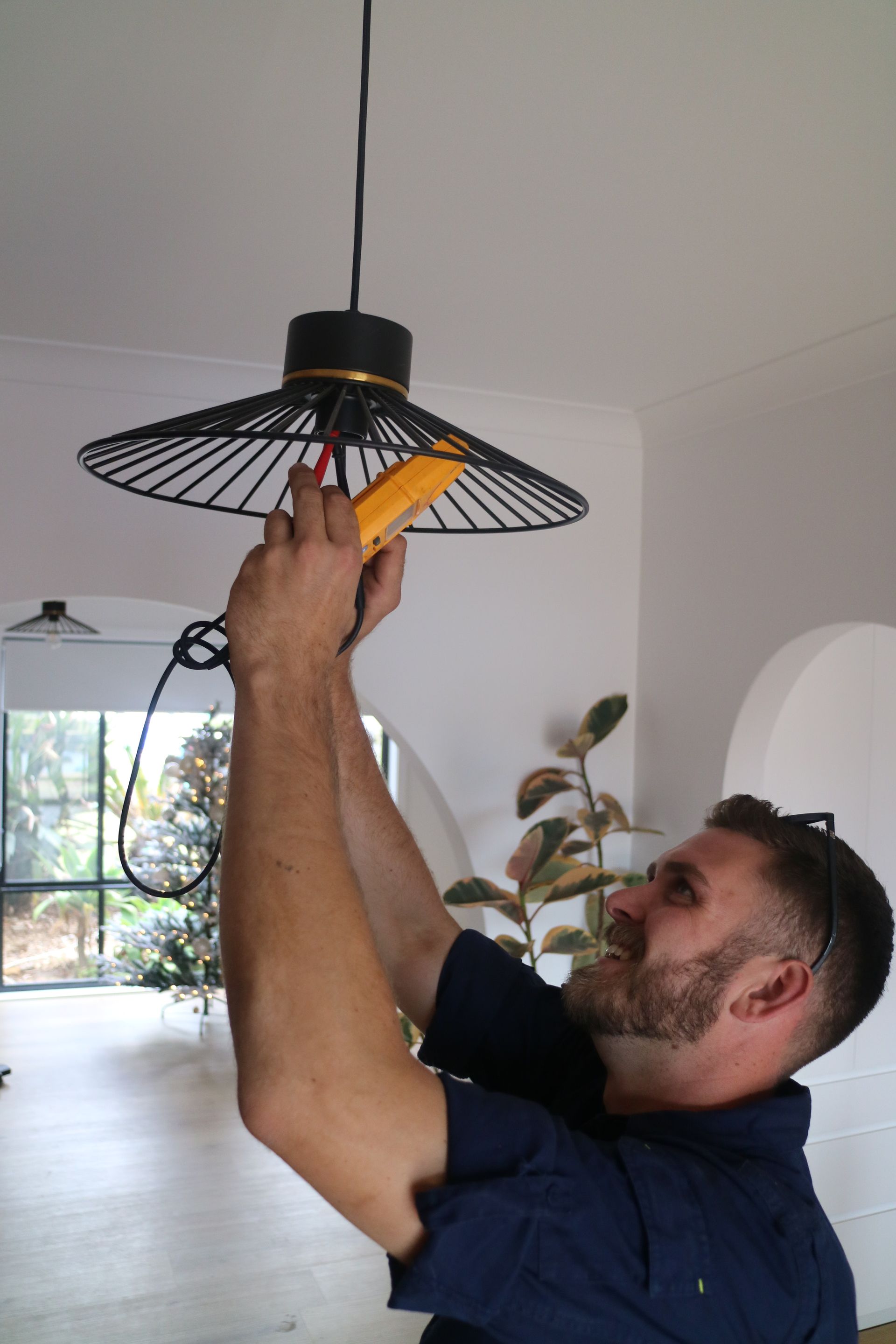 An Electrician Checking The Safety Of A Light Fixture— TB Electrical & Communications in Erina, NSW