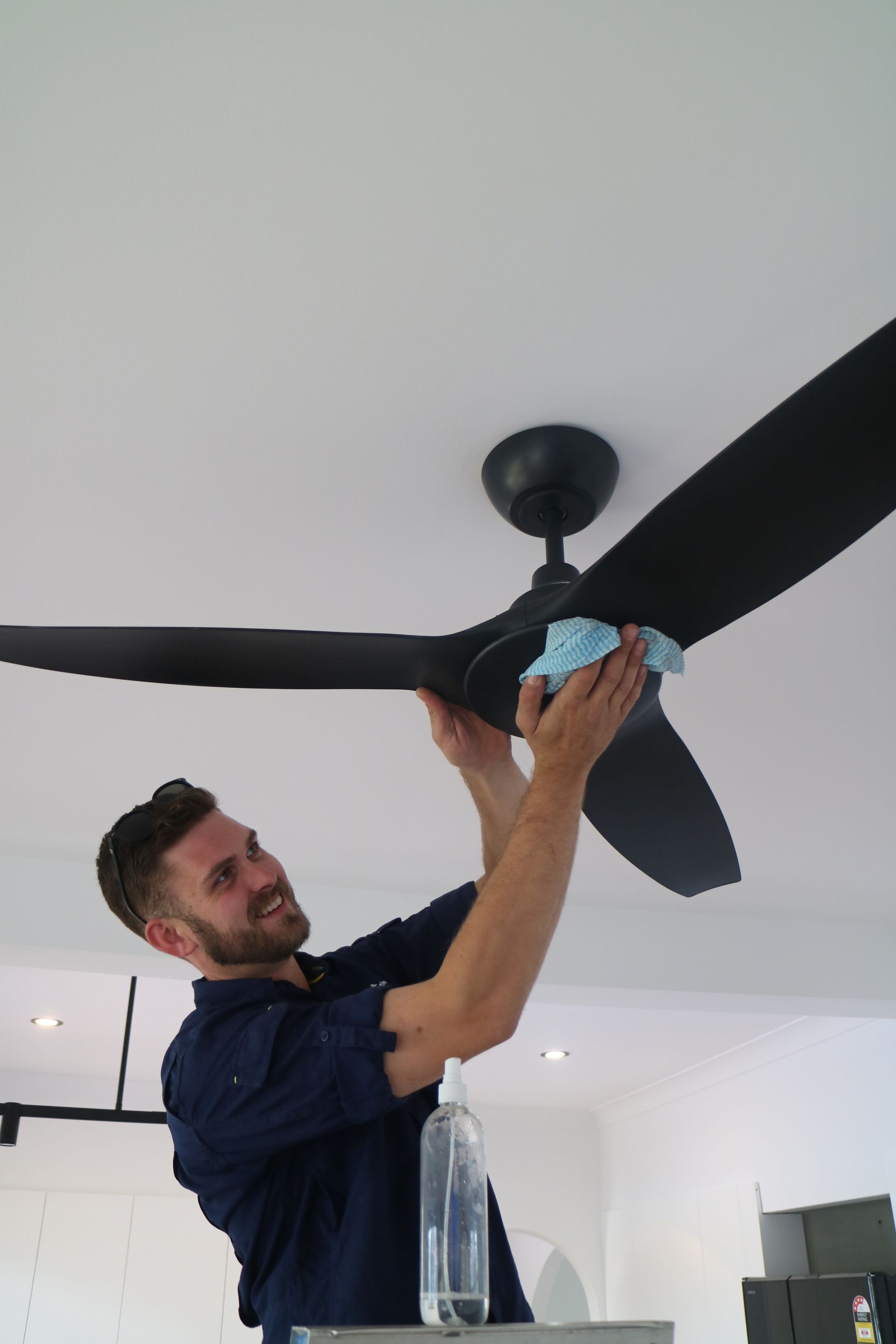 Electrician Cleaning A Ceiling Fan After Installation— TB Electrical & Communications in Erina, NSW