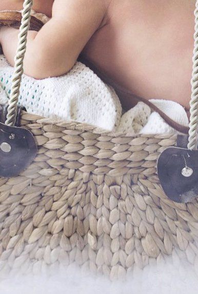 Baby in geflochtenem Korb, teilweise verdeckt, ruht auf weißer Decke. Seilgriff und schwarzes Metalldetail sichtbar.