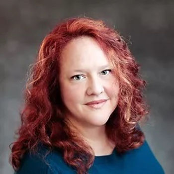Portrait of a smiling woman with curly red hair against a gray background
