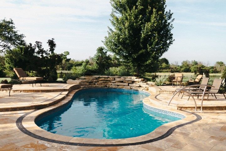 A large swimming pool is surrounded by chairs and a stone wall.