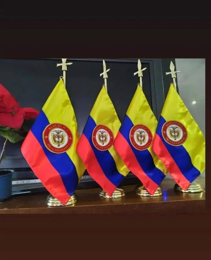 Cuatro pequeñas banderas con emblemas están alineadas sobre una mesa.