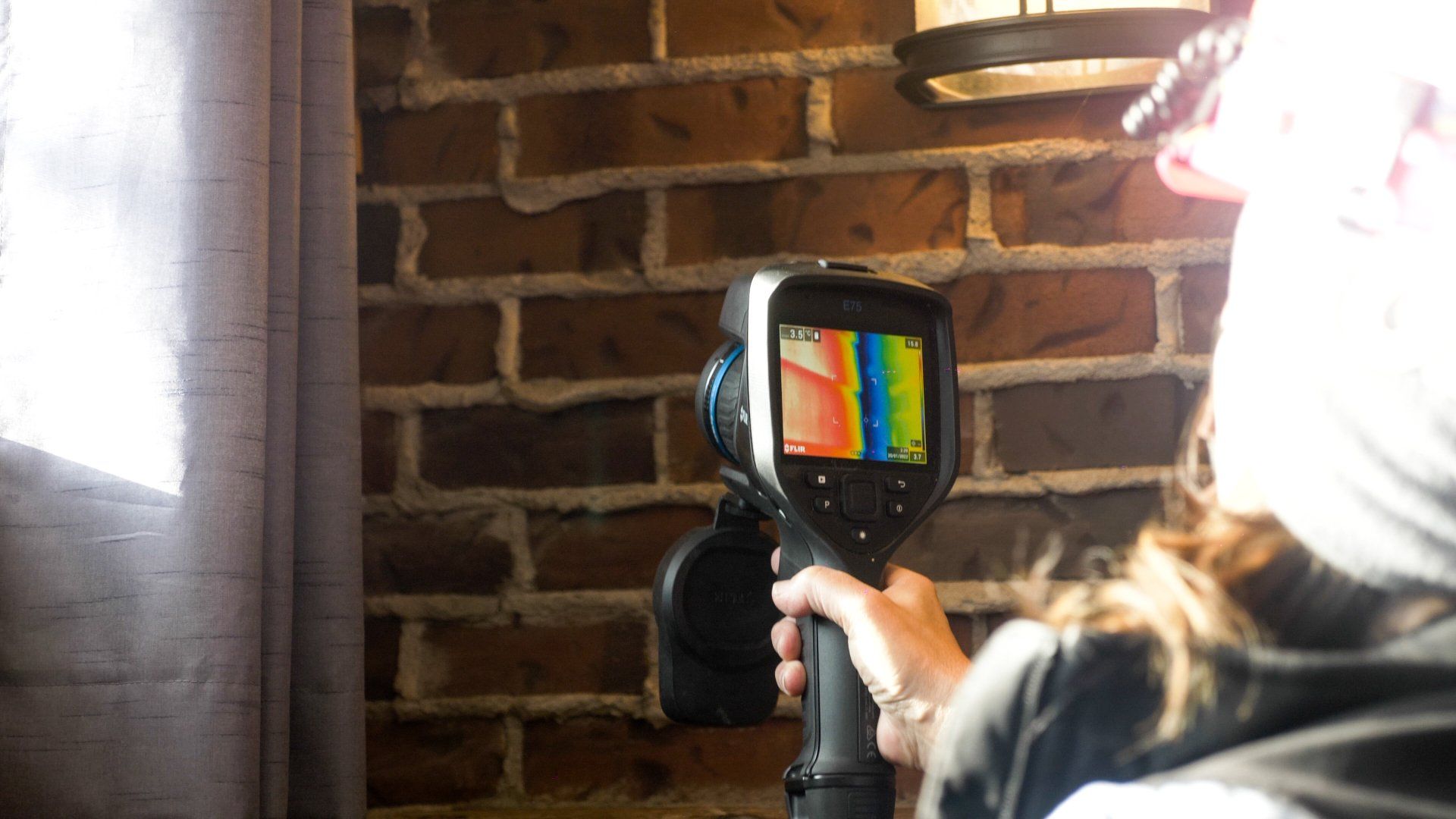 Personne utilisant une caméra thermique sur un mur de briques, affichant des variations de chaleur en couleur.