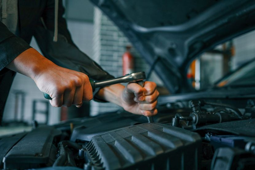 Mechanic using a ratchet wrench to work on an open car engine in a garage