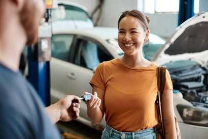 Woman smiling and receiving car keys from a dealership employee beside a car with its hood open