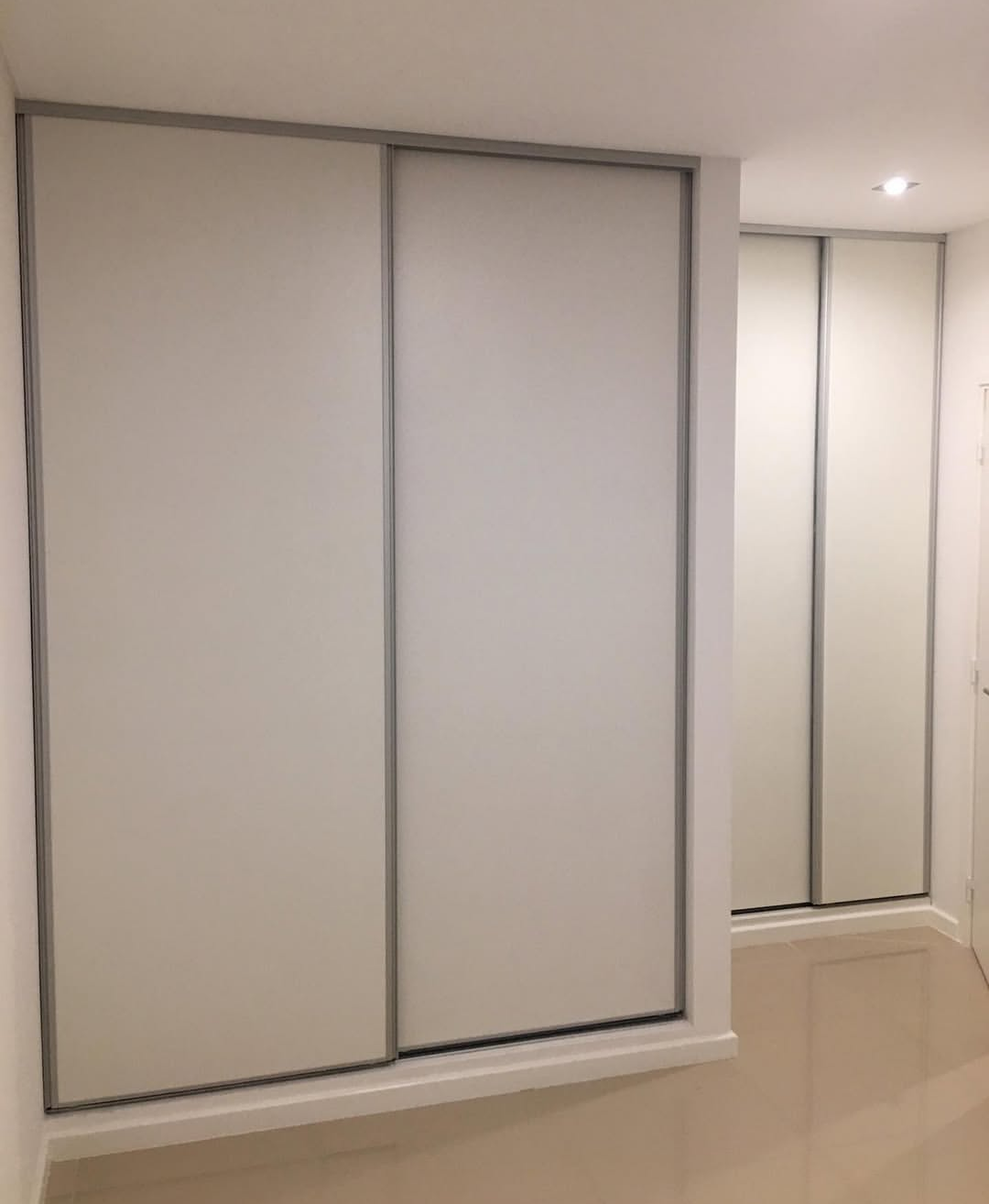Puertas corredizas de armario blancas con detalles plateados, en una habitación blanca con suelo de color claro.
