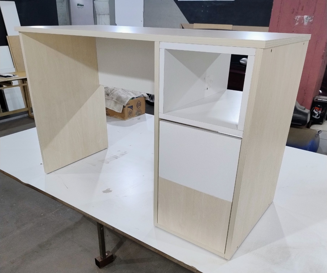 Escritorio de madera clara con mueble de almacenaje blanco a la derecha. Compartimento y cajón visibles.