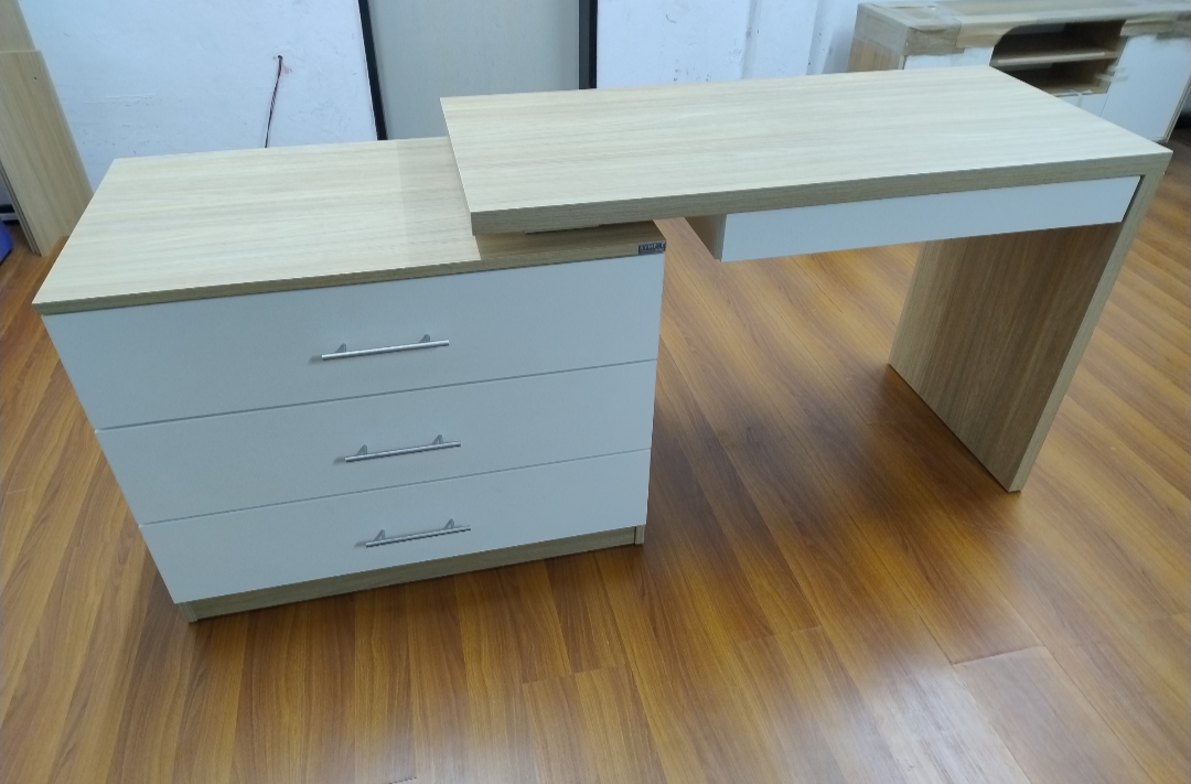 Escritorio de madera clara y color blanco con tres cajones sobre suelo de madera.