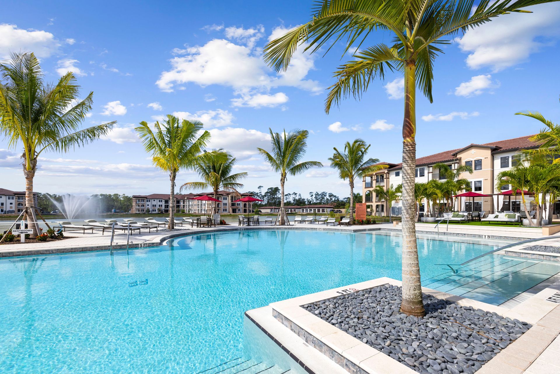 A large swimming pool surrounded by palm trees and buildings at Corsa at Estero Crossing.