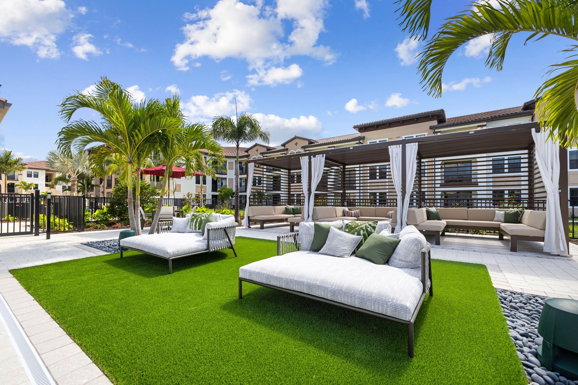 A lush green lawn with white couches and chairs in front of a building at Corsa at Estero Crossing.