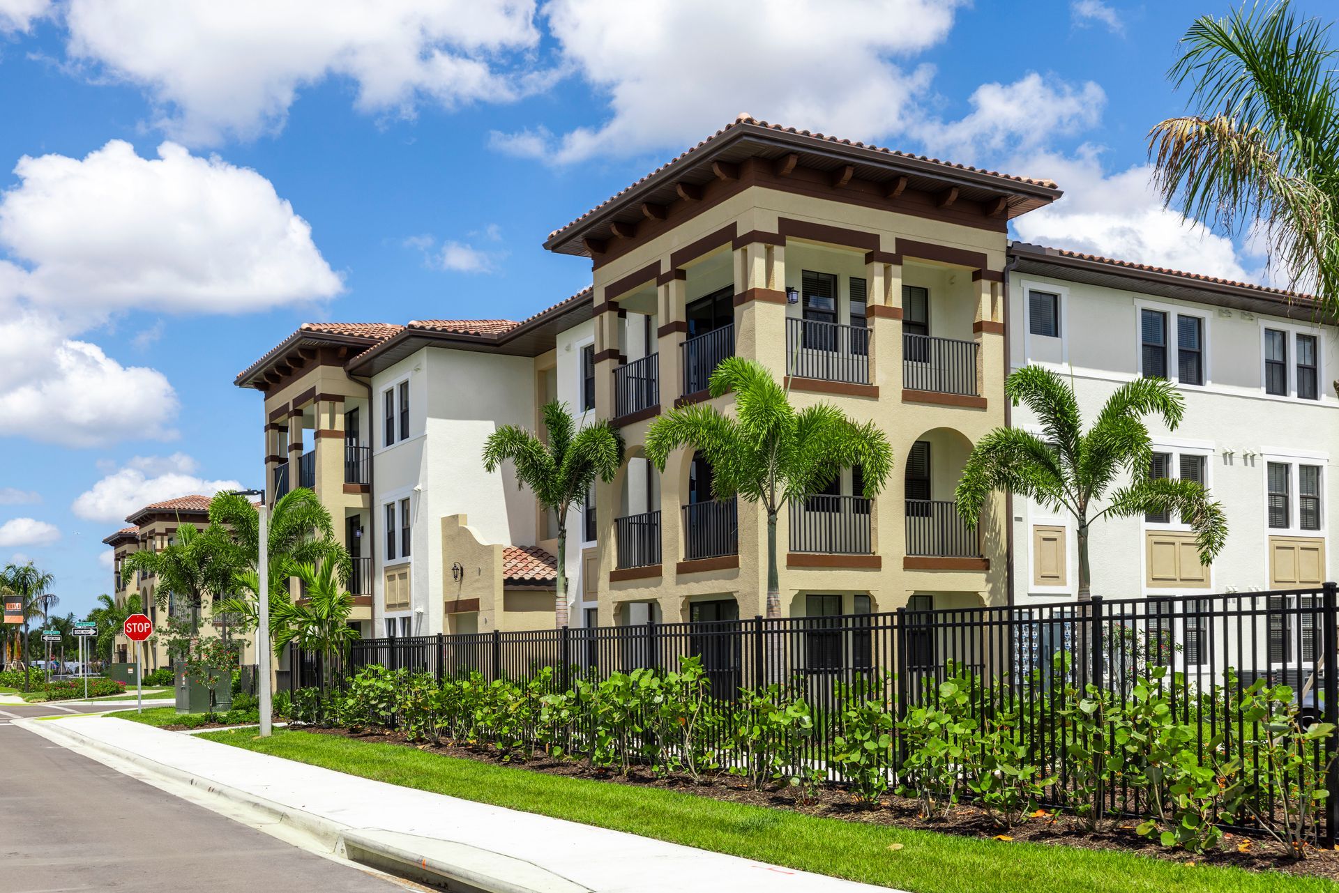 A large apartment building with a fence and palm trees in front of it at Corsa at Estero Crossing.
