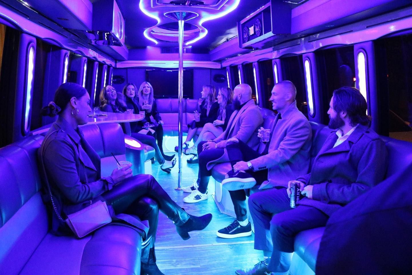 A group of people are sitting on purple couches in a party bus.