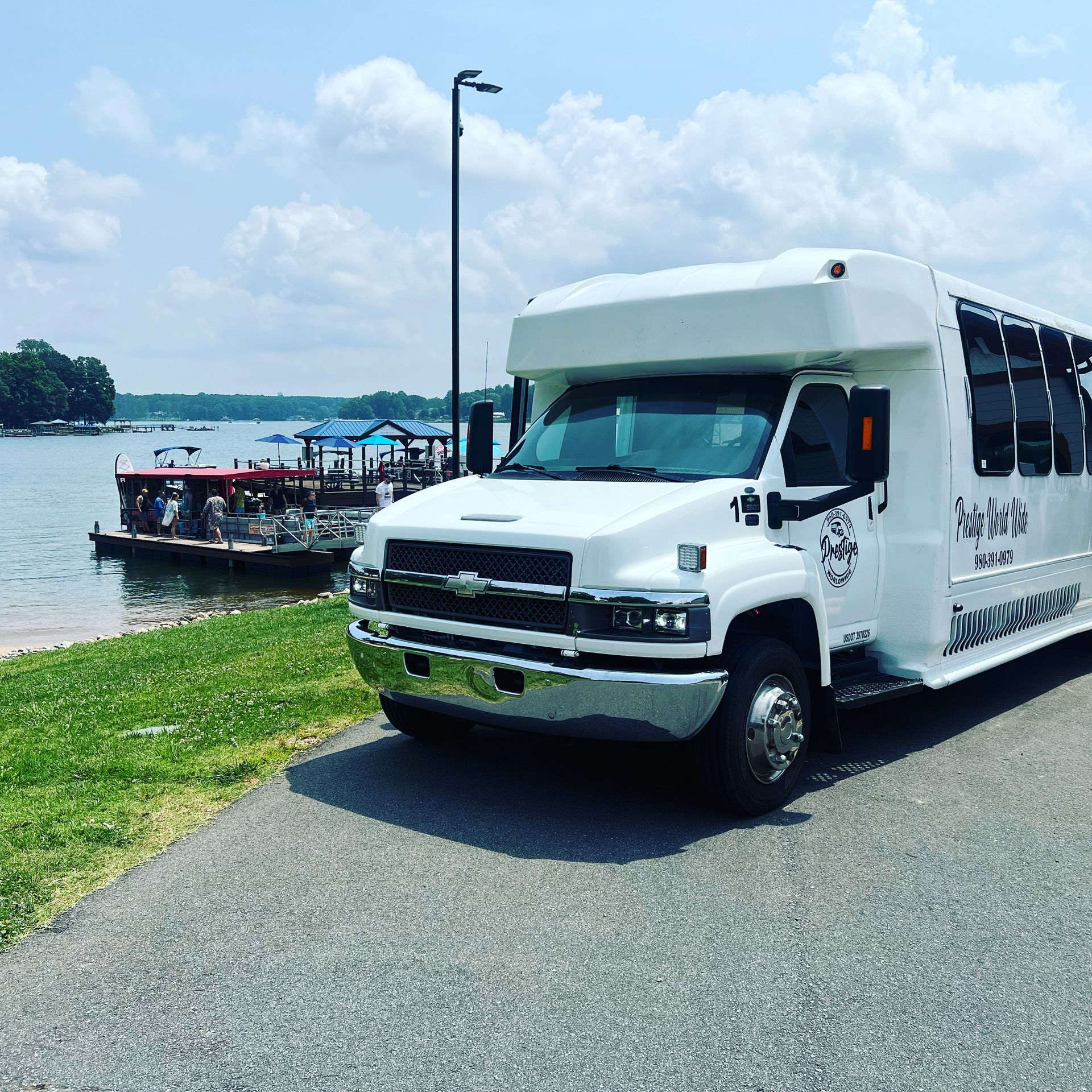 A white bus is parked on the side of the road next to a body of water.