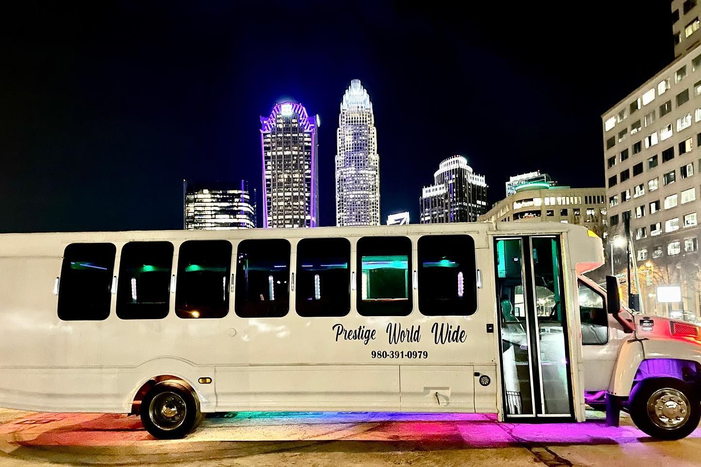 A white party bus is parked in front of a city skyline at night.