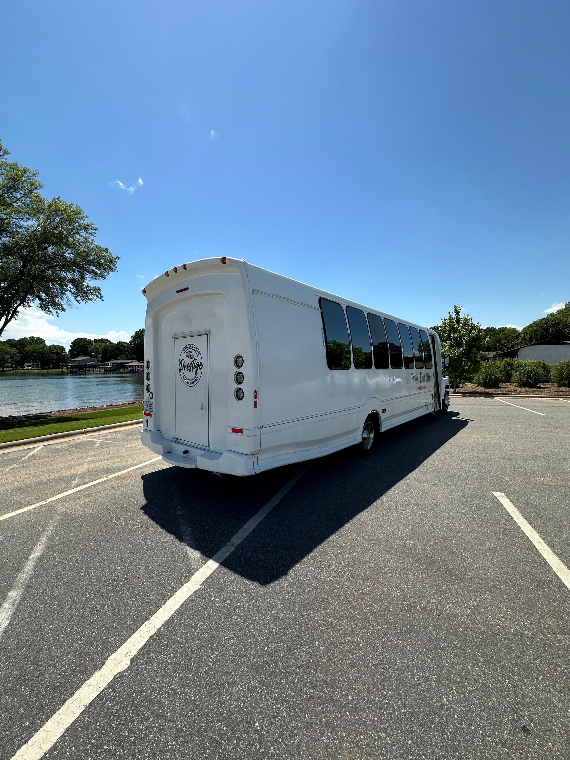 A white bus is parked in a parking lot next to a body of water.