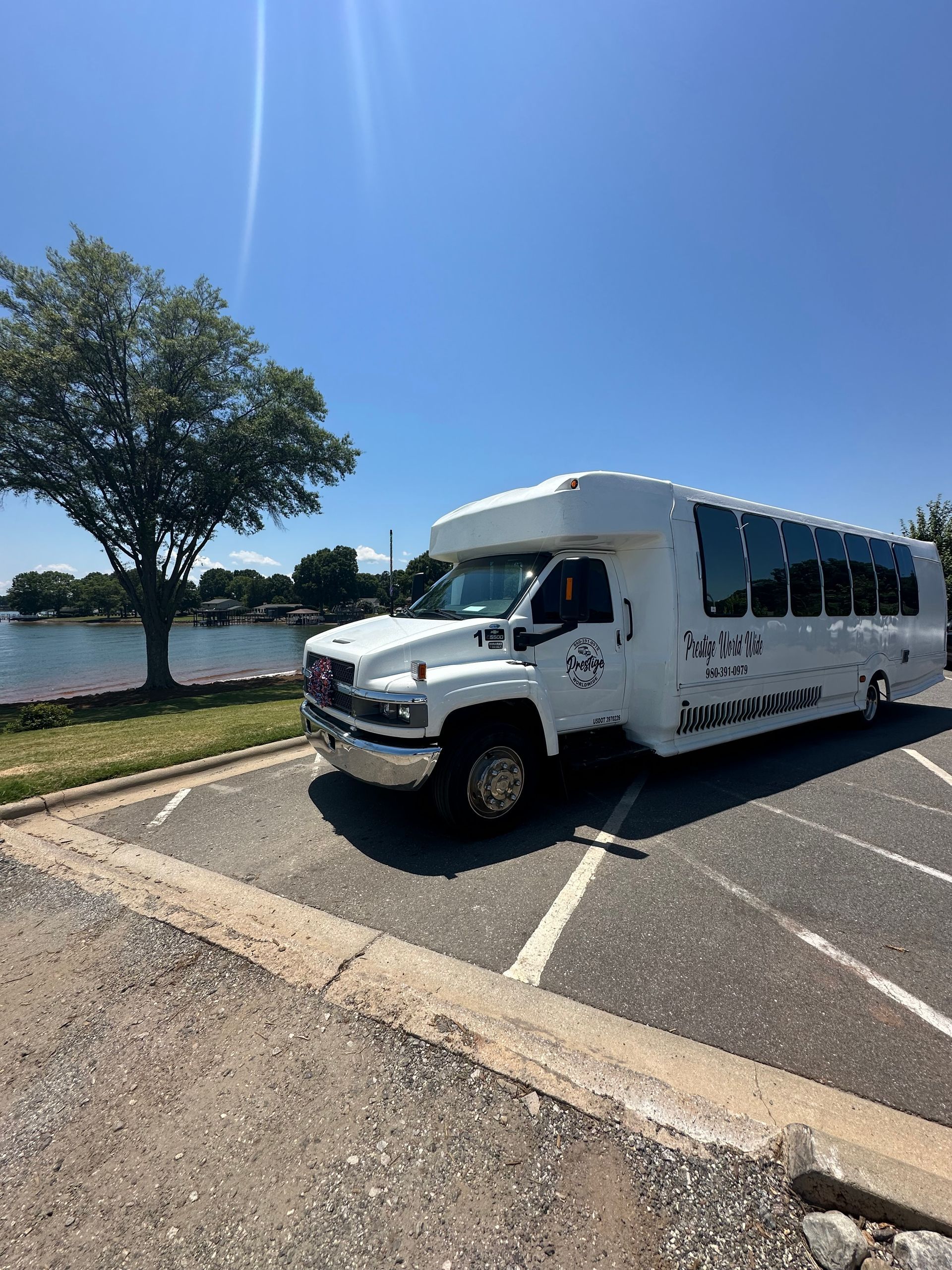 A white bus is parked in a parking lot next to a body of water.