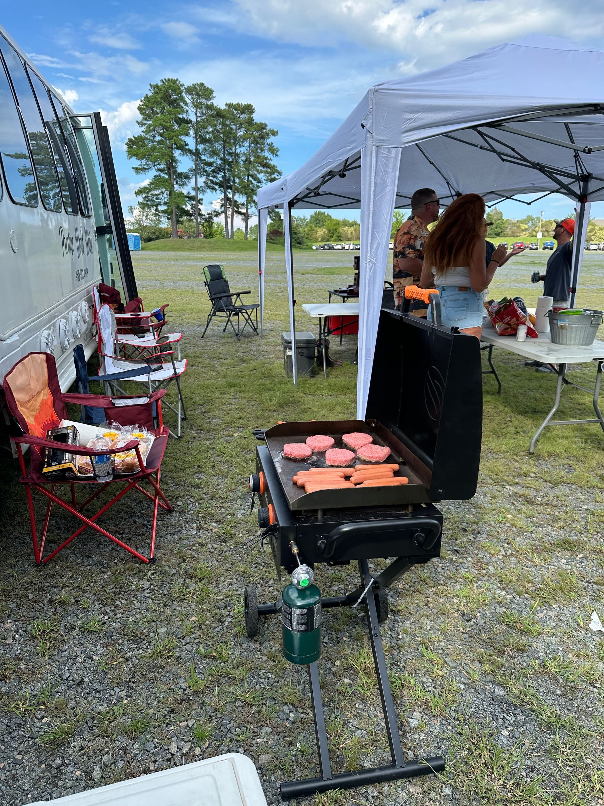 A group of people are standing around a grill in a field.