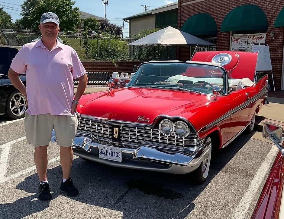 A picture of Dr. Brill next to a classic red car.
