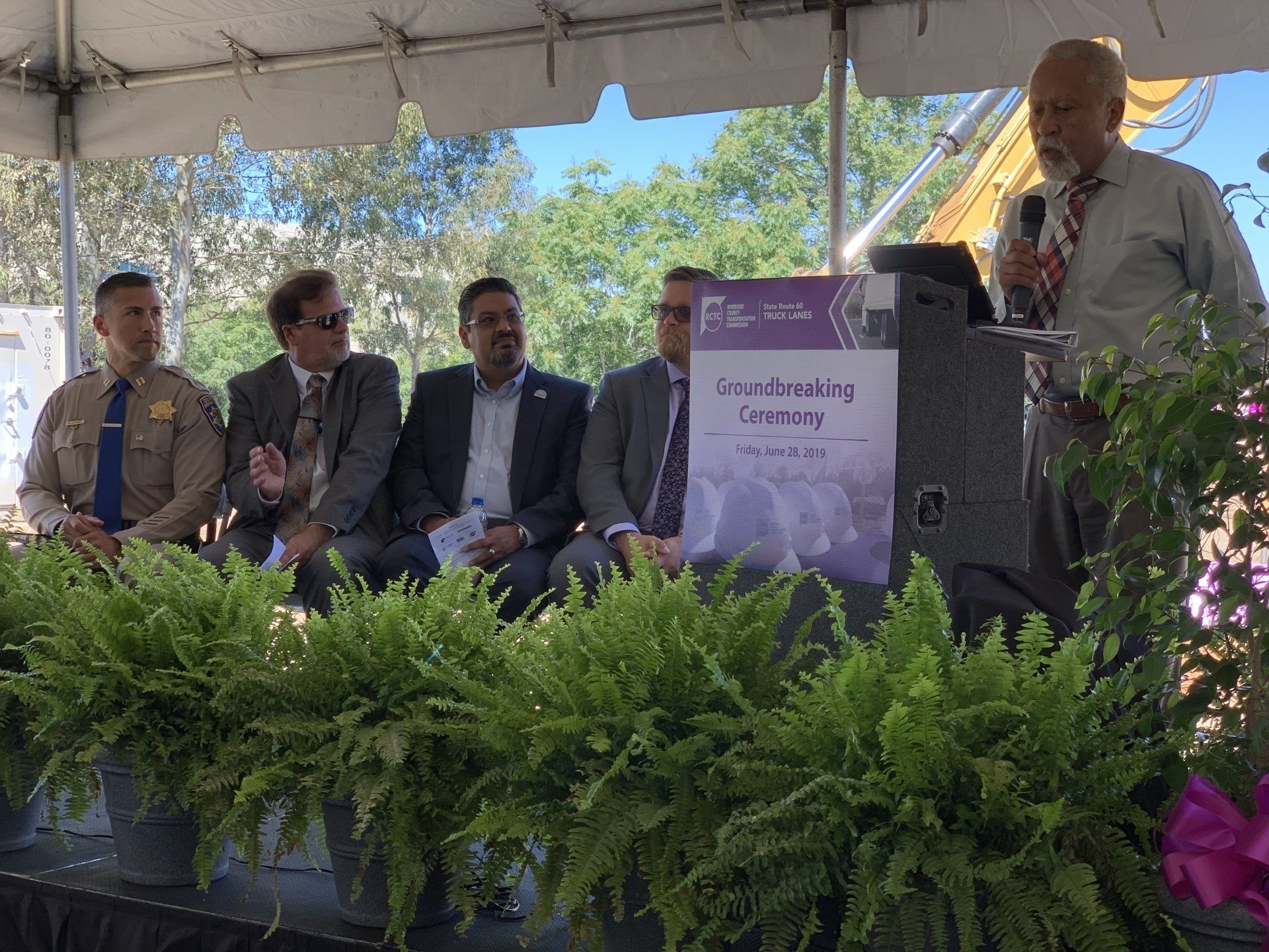 A group of men are sitting on a stage under a tent.