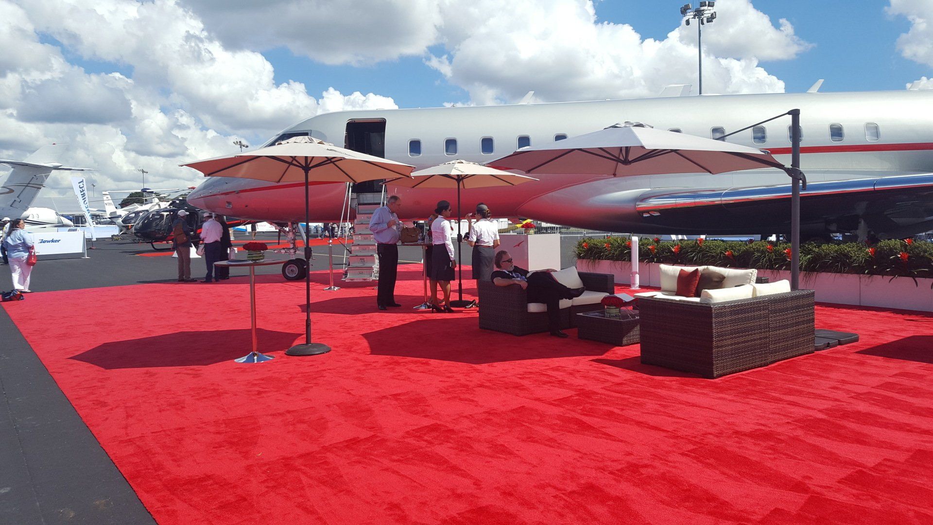 A red carpet with umbrellas and a plane in the background