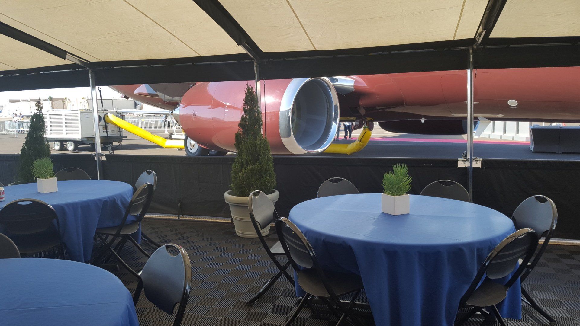 Tables and chairs under a tent with a plane in the background