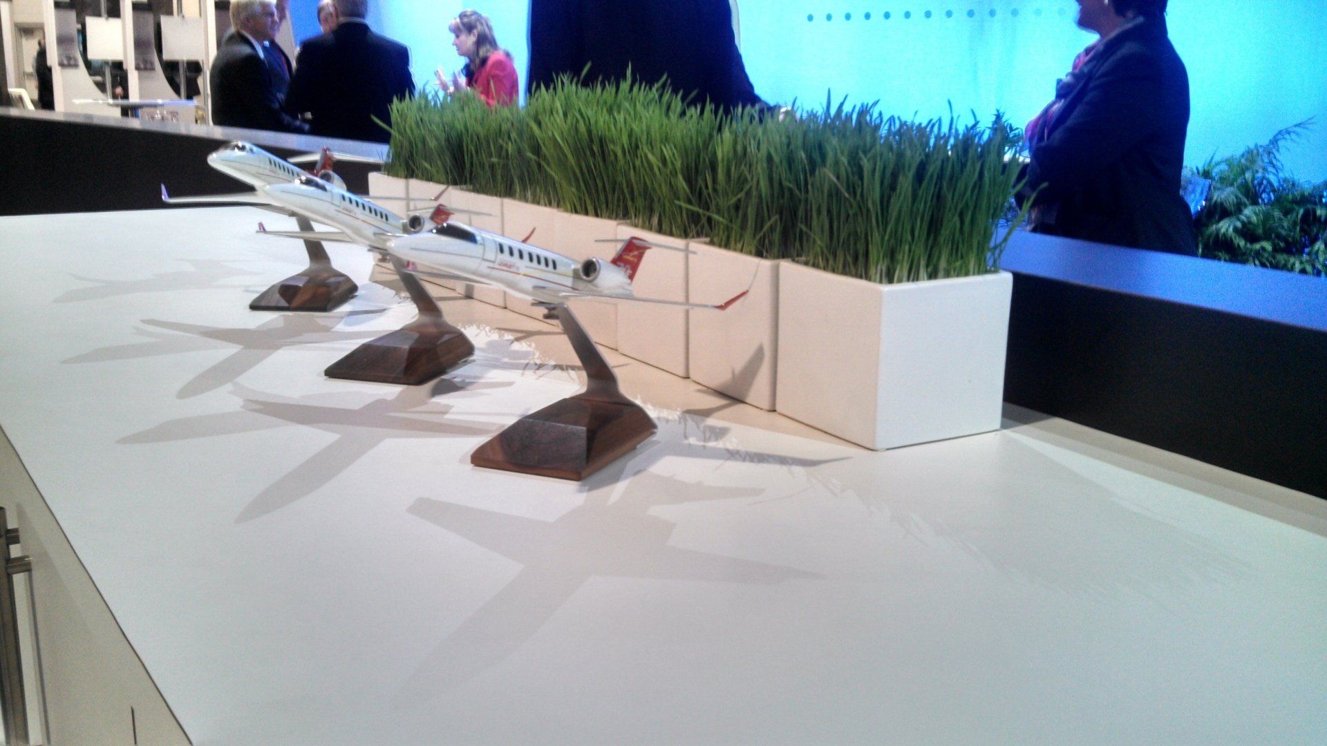 A model airplane sits on a table next to a planter of grass