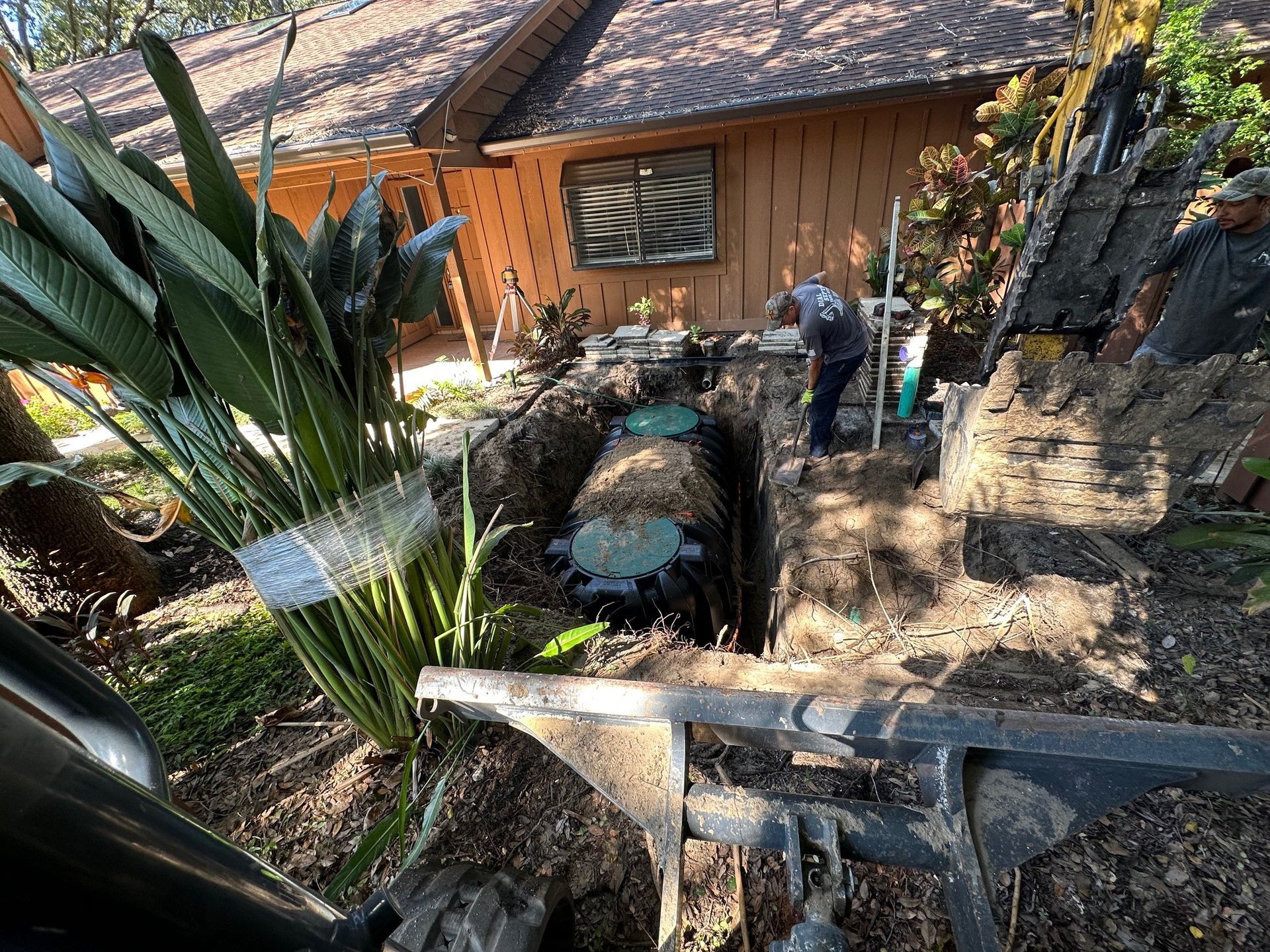 Men working on a septic tank in a yard with a house in the background.