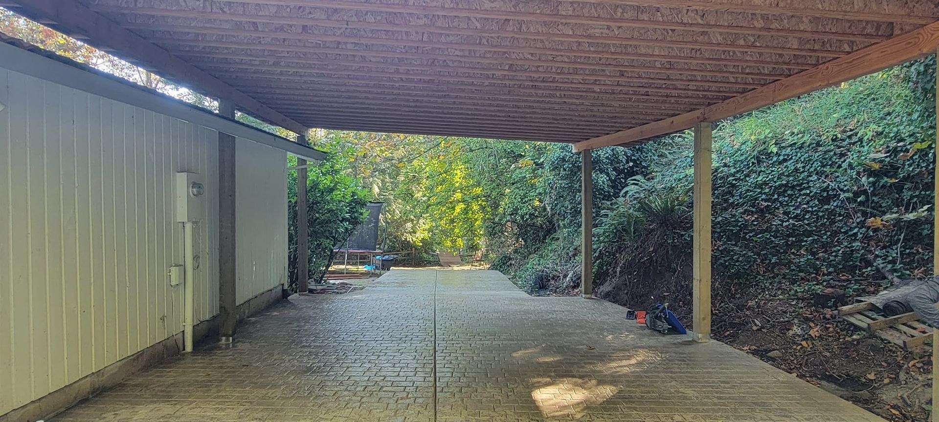 A carport with a wooden roof and trees in the background.
