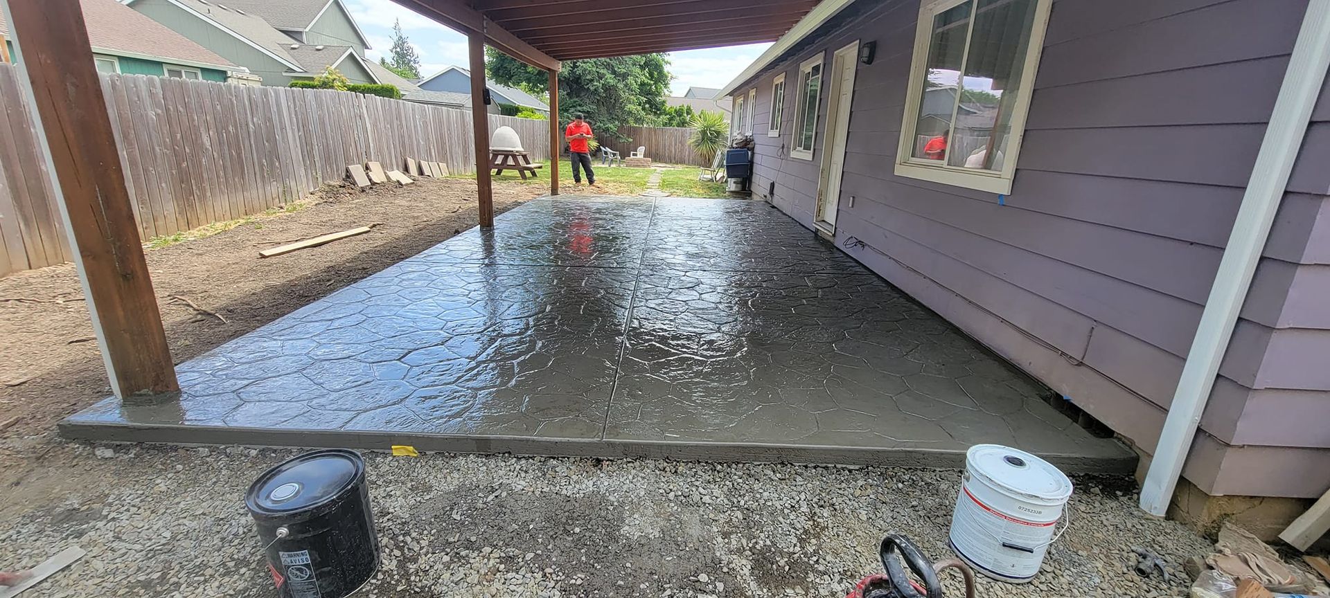 A concrete patio is being built in the backyard of a house.