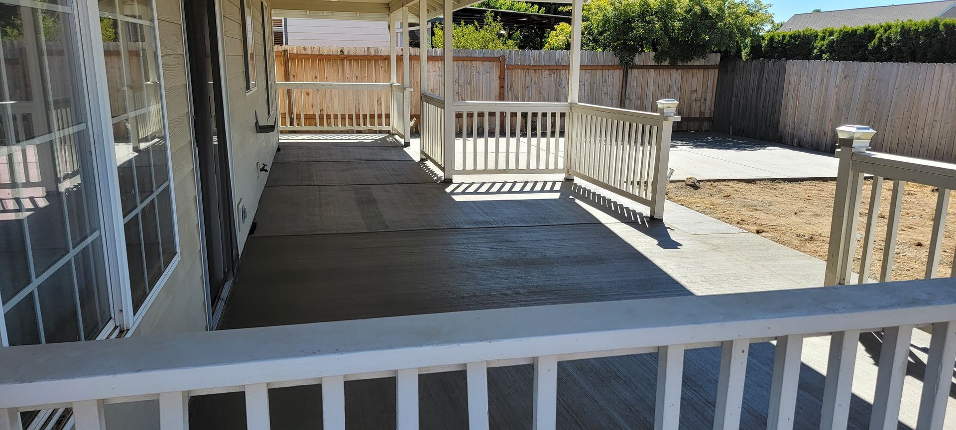 An empty porch with a white railing and a fence in the background.