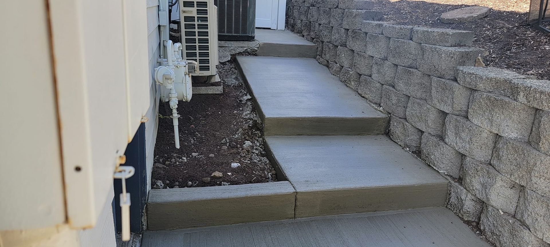 A concrete walkway leading up to a house next to a stone wall.