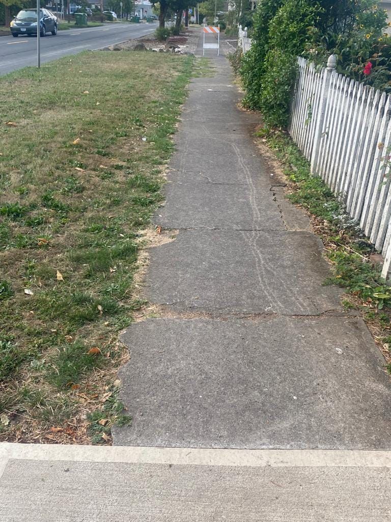 A sidewalk with a white picket fence along the side of it.