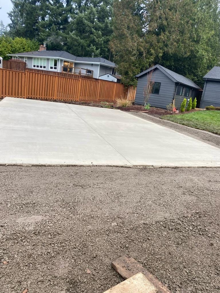 A concrete driveway with a wooden fence and a house in the background.
