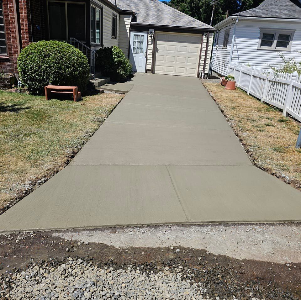 A concrete driveway leading to a house with a white fence