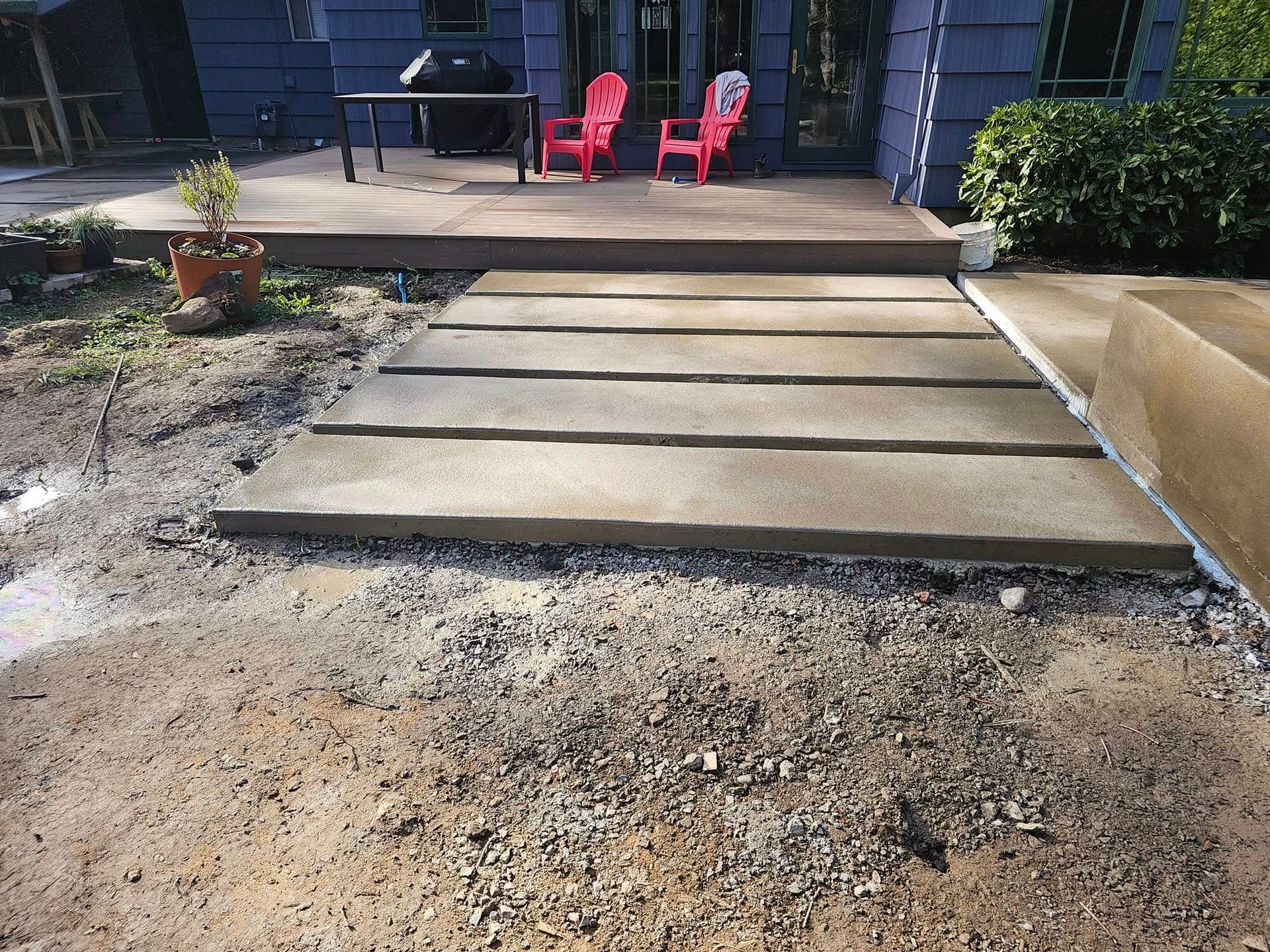 A concrete walkway leading to a deck with red chairs