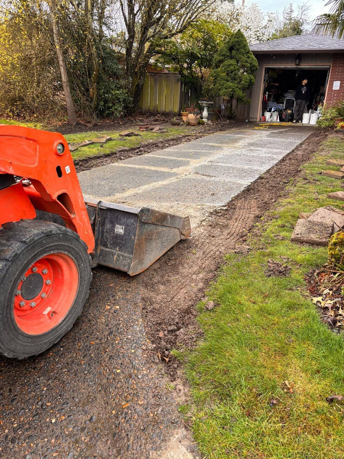 A tractor is driving down a dirt road next to a garage.