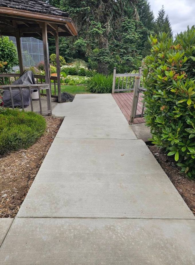 A concrete walkway leading to a gazebo in a garden.