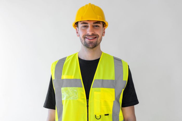 A man wearing a yellow hard hat and a yellow vest is smiling.