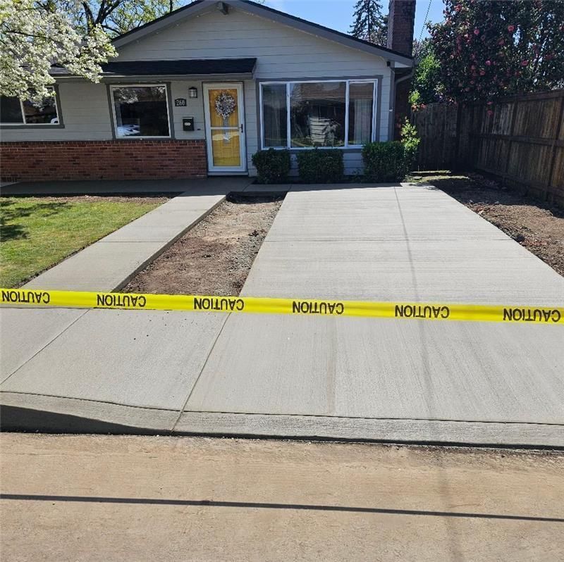 A concrete driveway with a fence and a house in the background.