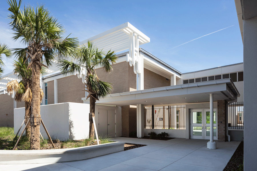 A modern building with a red and gray facade and a glass wall under a blue sky.