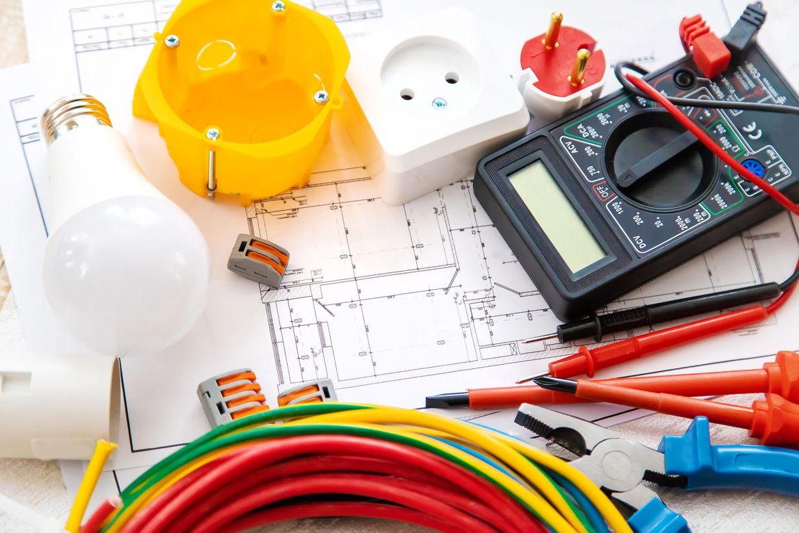 Electrical tools and components on a blueprint: multimeter, wires, light bulb, outlet, junction box.